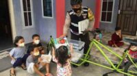 Bripka Samson Tarigan, Bhabinkamtibmas Kelurahan Darussalam, Kecamatan Meral Barat tengah membagikan buku-buku bacaan kepada anak-anak di wilayah operasionalnya.